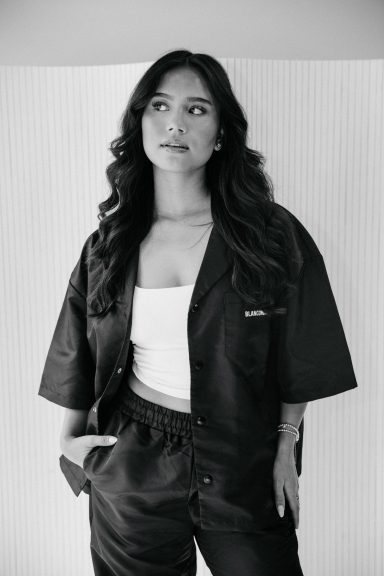 Vrouw met lange, golvende haren in een zwart outfit, kijkend naar de camera.