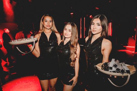 Drie vrouwen in zwarte jurken met schalen, poseren in een sfeervolle omgeving.
