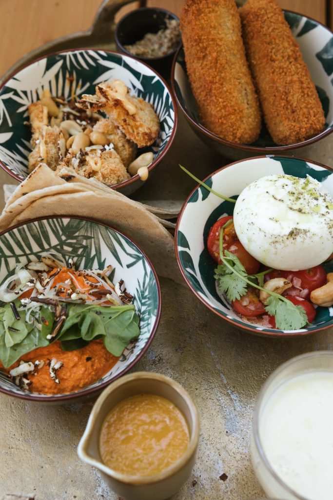 Een tafelsetting met kleurrijke gerechten: salades, kroketten, saus en een yoghurtachtige dip.