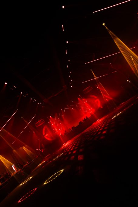 Donker evenement met rood en geel licht, stralen en een feestelijke sfeer.