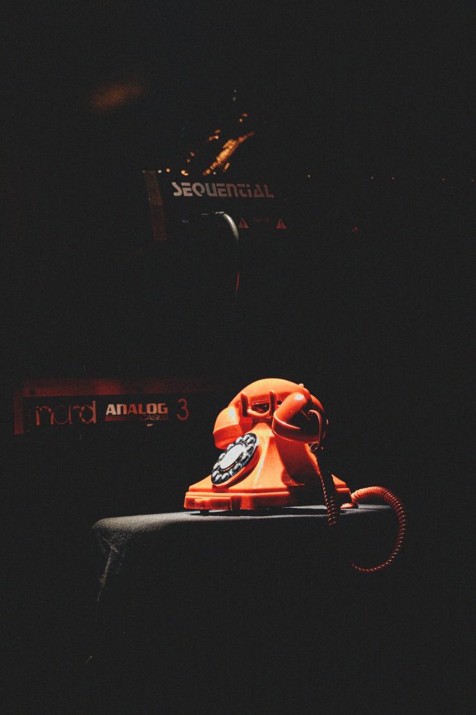 Jair Faria Bitterzoet Amsterdam Een vintage oranje telefoon op een donkere achtergrond.