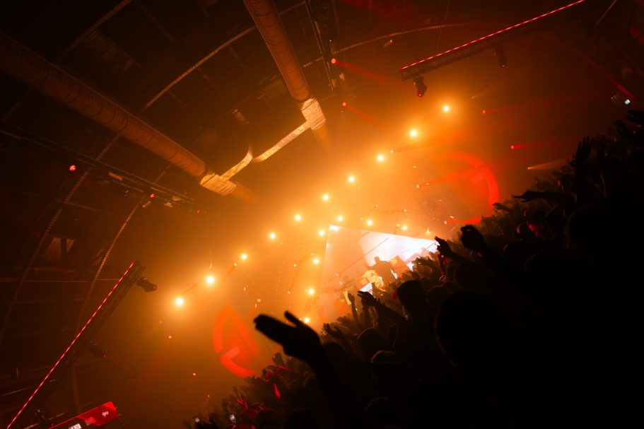 Lichten stralen door een druk indoor concert met opgewonden mensen.