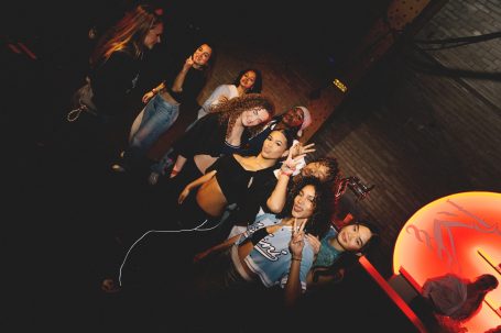 Groep jongeren poseert vrolijk in een sfeervolle nachtclubomgeving.