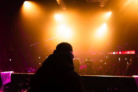 Silhouet van een persoon achter het DJ-tafel met felgekleurde lichten op de achtergrond.
