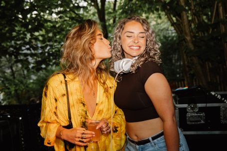 DJ H4zel - Geheime Liefde Festival Twee vrouwen poseren op een festival, één geeft een kus op de wang van de ander.