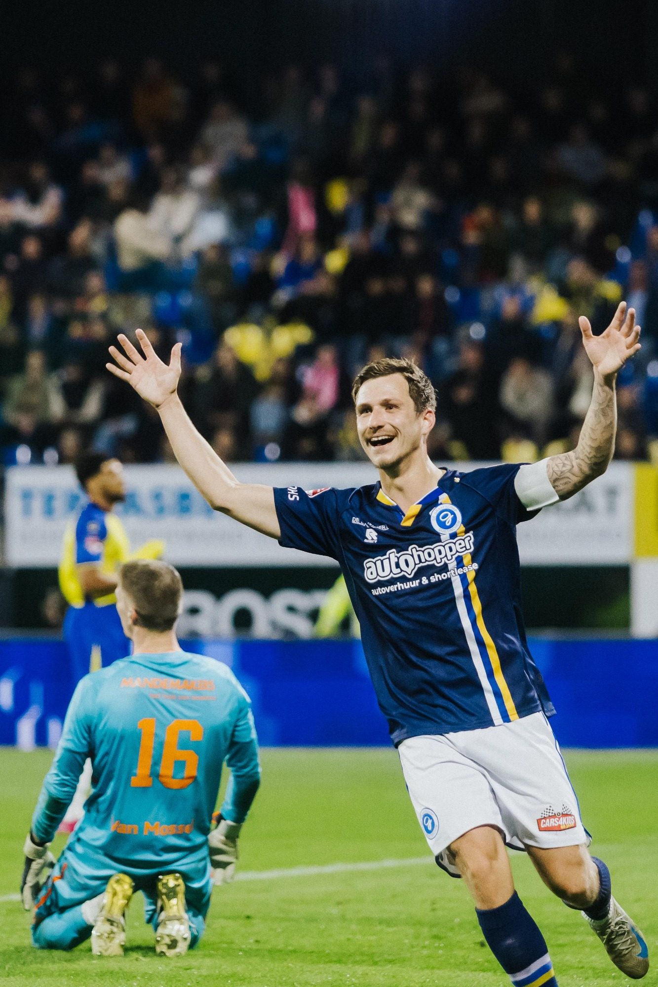 Gelukkige voetballer juicht na het scoren van een doelpunt, terwijl de keeper achter hem zit.