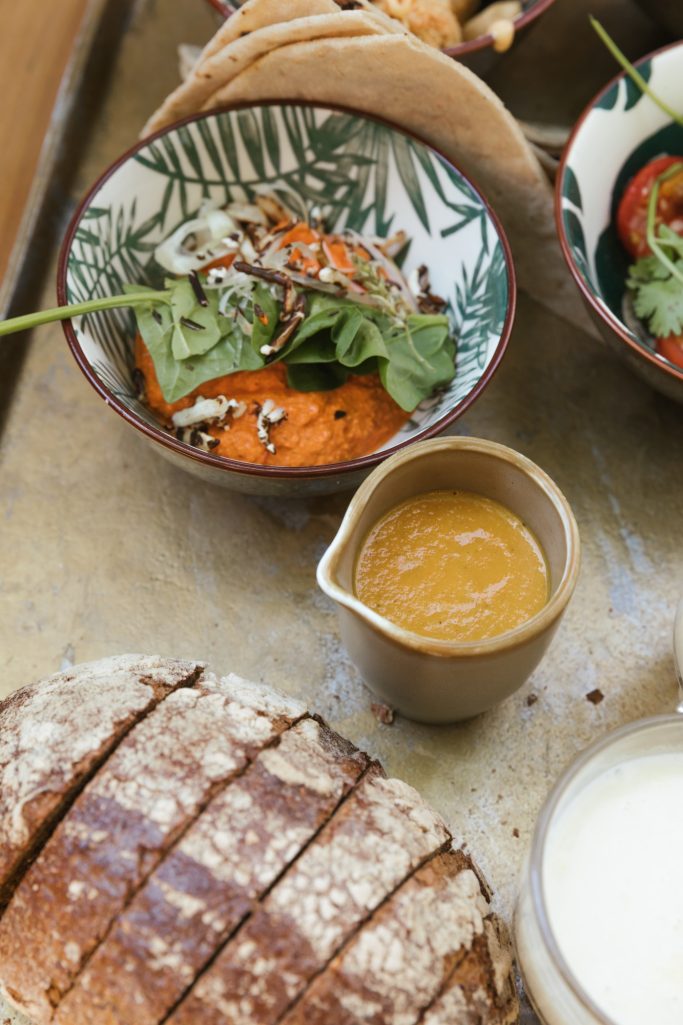 Een schotel met gebakken zoete aardappel, salade en saus, naast een stuk volkorenbrood.