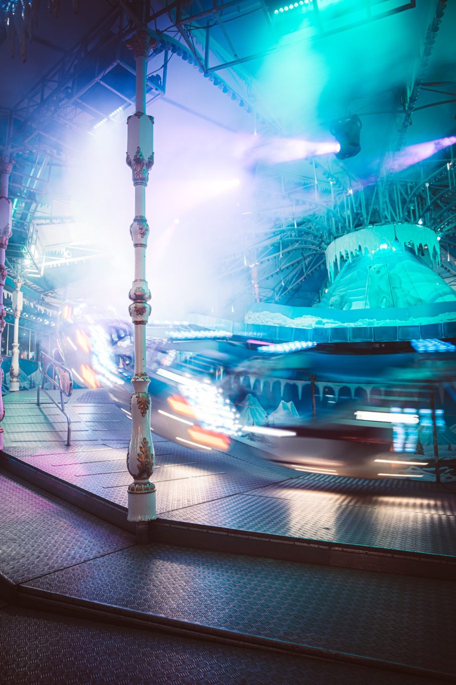 Kermisattractie met kleurrijke lichten en bewegende voertuigen in een nachtelijke setting.