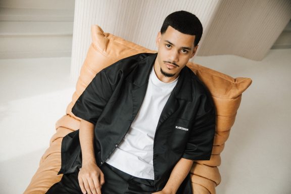 Een man in een zwart shirt zit op een grote, oranje kussen.