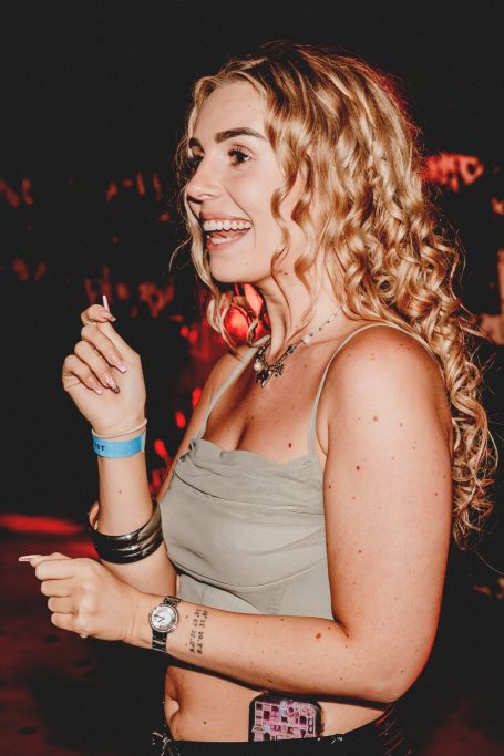 Jonge vrouw met krullend blond haar, lachend en genietend op een evenement.