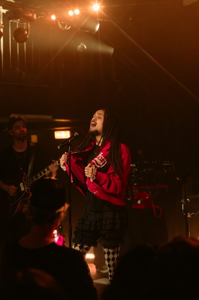 Jair Faria Bitterzoet Amsterdam Zangeres met lange, donkere haren in een felgekleurde outfit op het podium tijdens een concert.