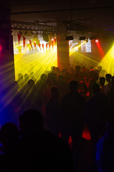Mensen dansen in een fel verlichte ruimte met kleurrijke lichtstralen.