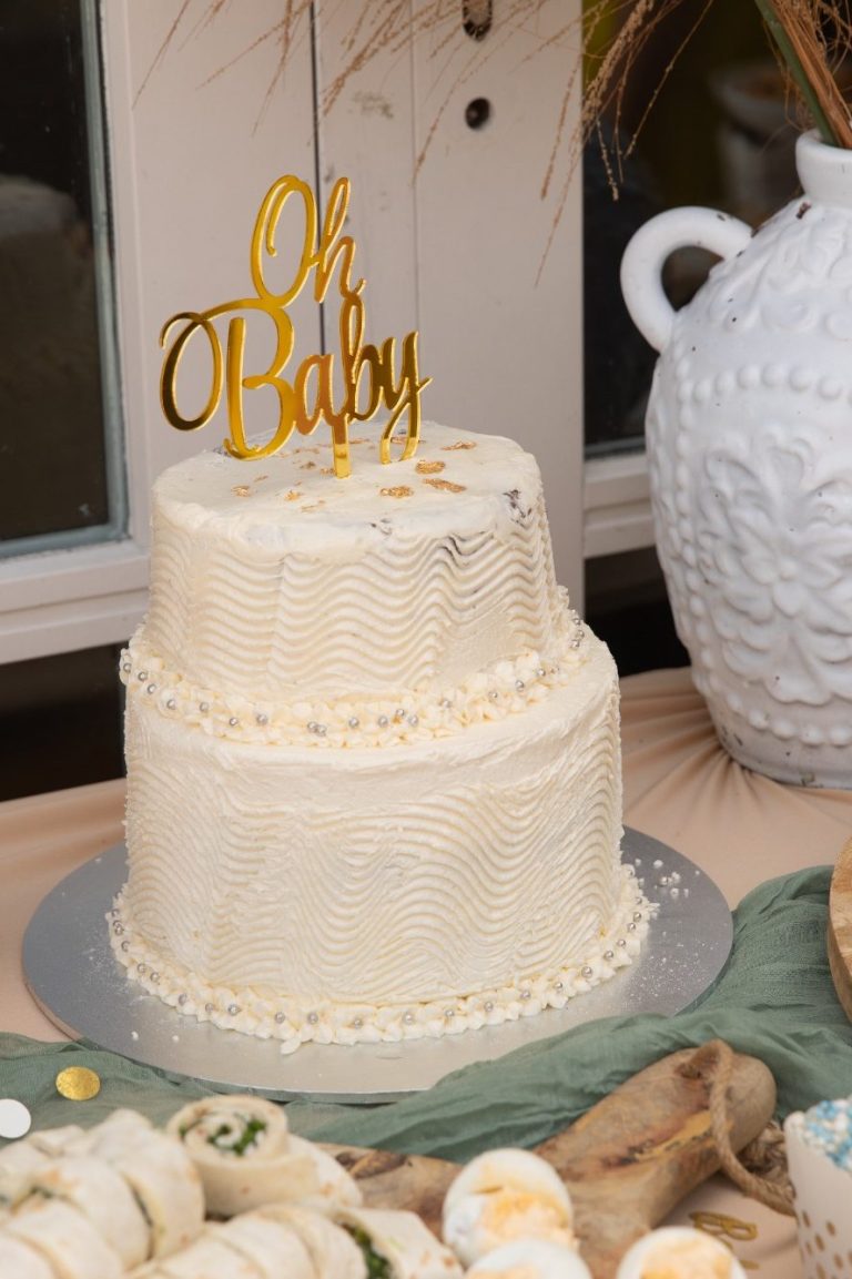 Een twee-laags witte babytaart met een gouden "Oh Baby" topper.