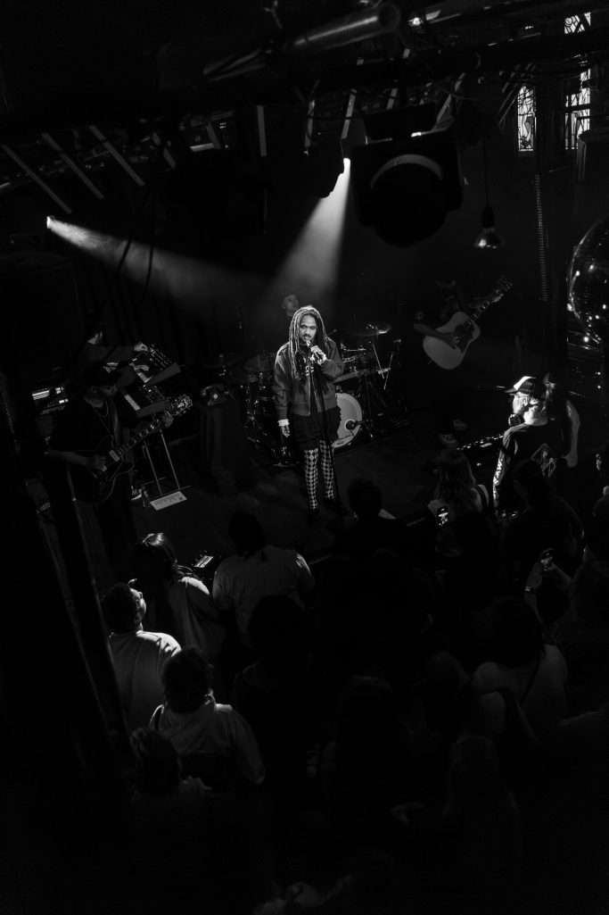 Jair Faria Bitterzoet Amsterdam Crowd Zwart-wit foto van een live muziekoptreden met een zanger op het podium.