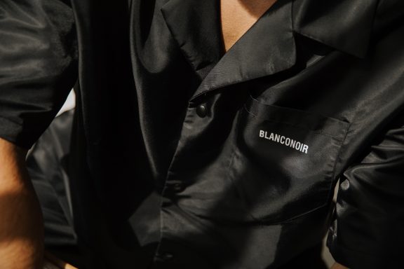 Zwart satijnen overhemd met logo op de borst.