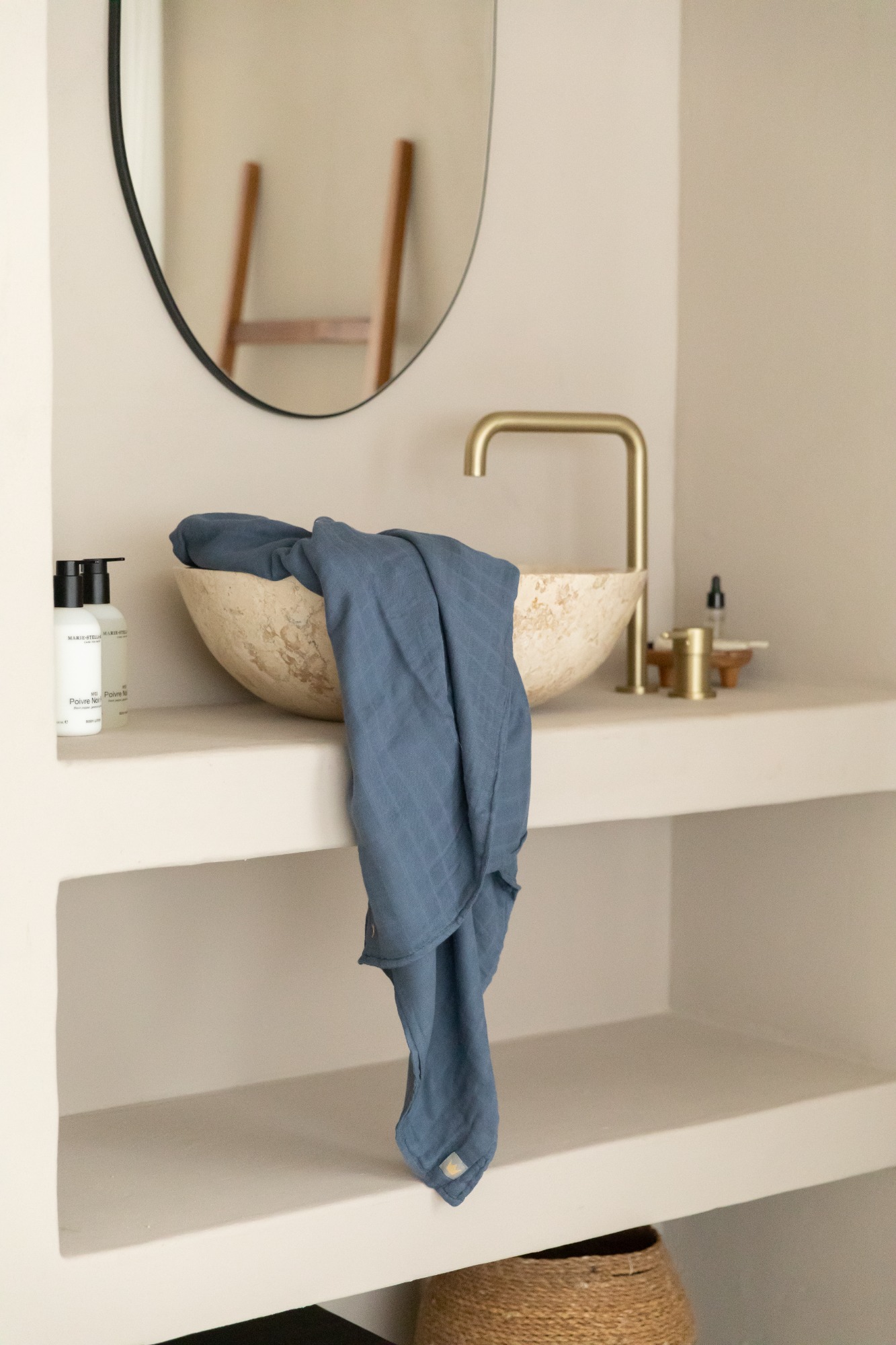 Witte schaal met een blauwe doek op een plank, naast een spiegel en accessoires.