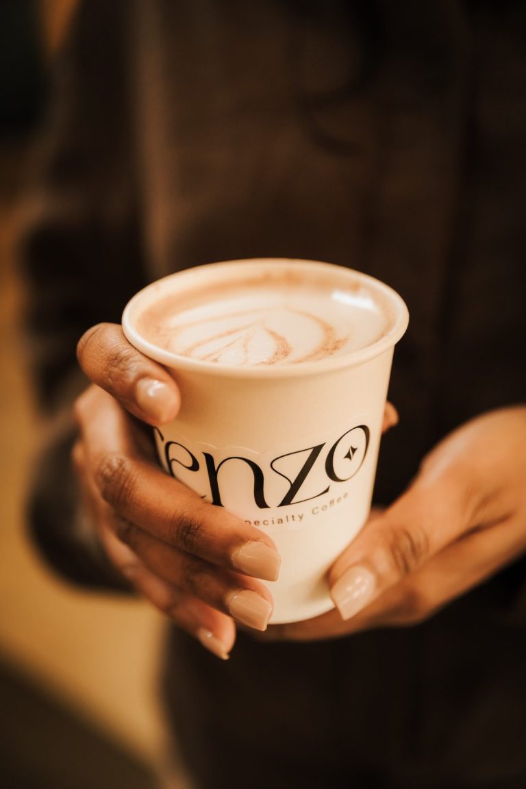 Hand houdt een mok met cappuccino en een mooi schuimpatroon.