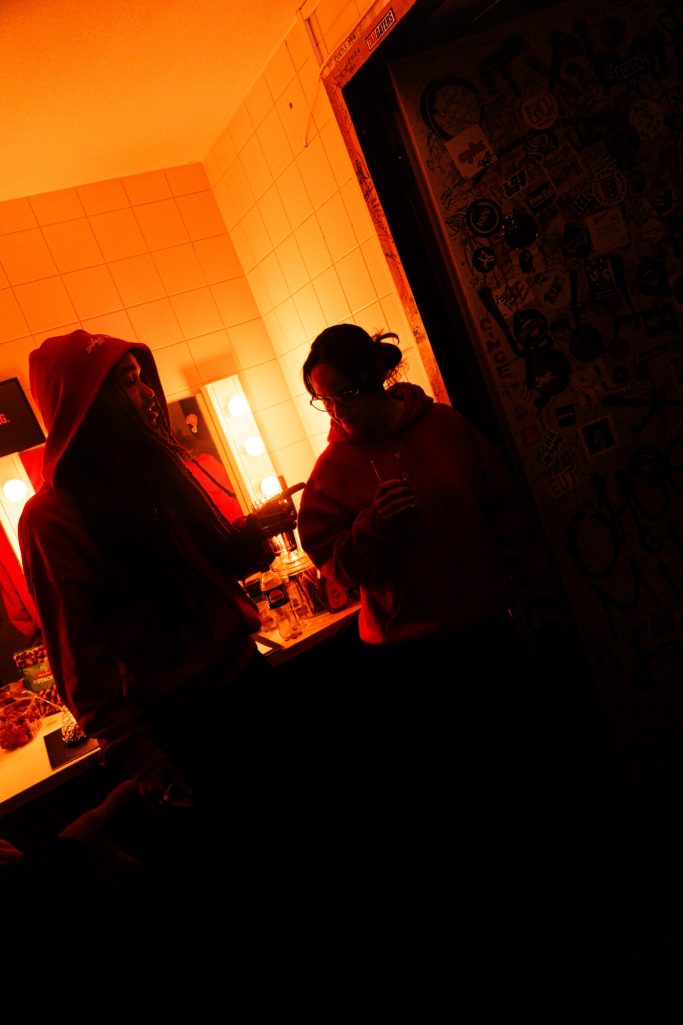 Jair Faria Bitterzoet Amsterdam BTS Twee personen in een slecht verlichte kamer, gekleed in hoodies en petten.