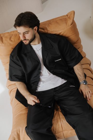 Man in casual black outfit sitting on a large, soft, light-colored pillow.