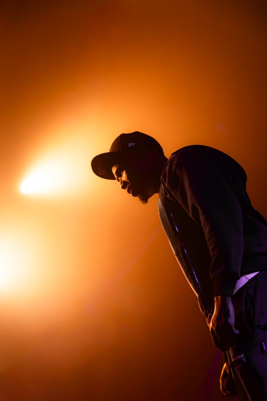Silhouet van een man met een cap, verlicht door oranje lichtstralen.