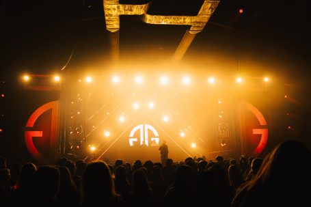 Een concert met een podium vol lichten en een menigte vooraan.