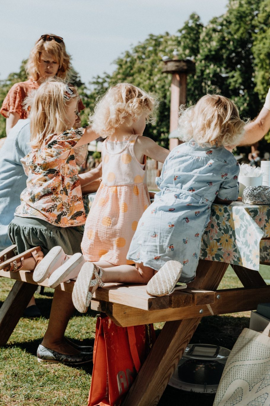 Drie kinderen met blonden haren staan bij een tuinset met een tafel vol spullen.
