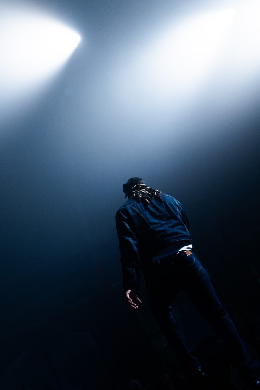 Een persoon in donkere kleding staat in een mistige ruimte met lichtstralen.