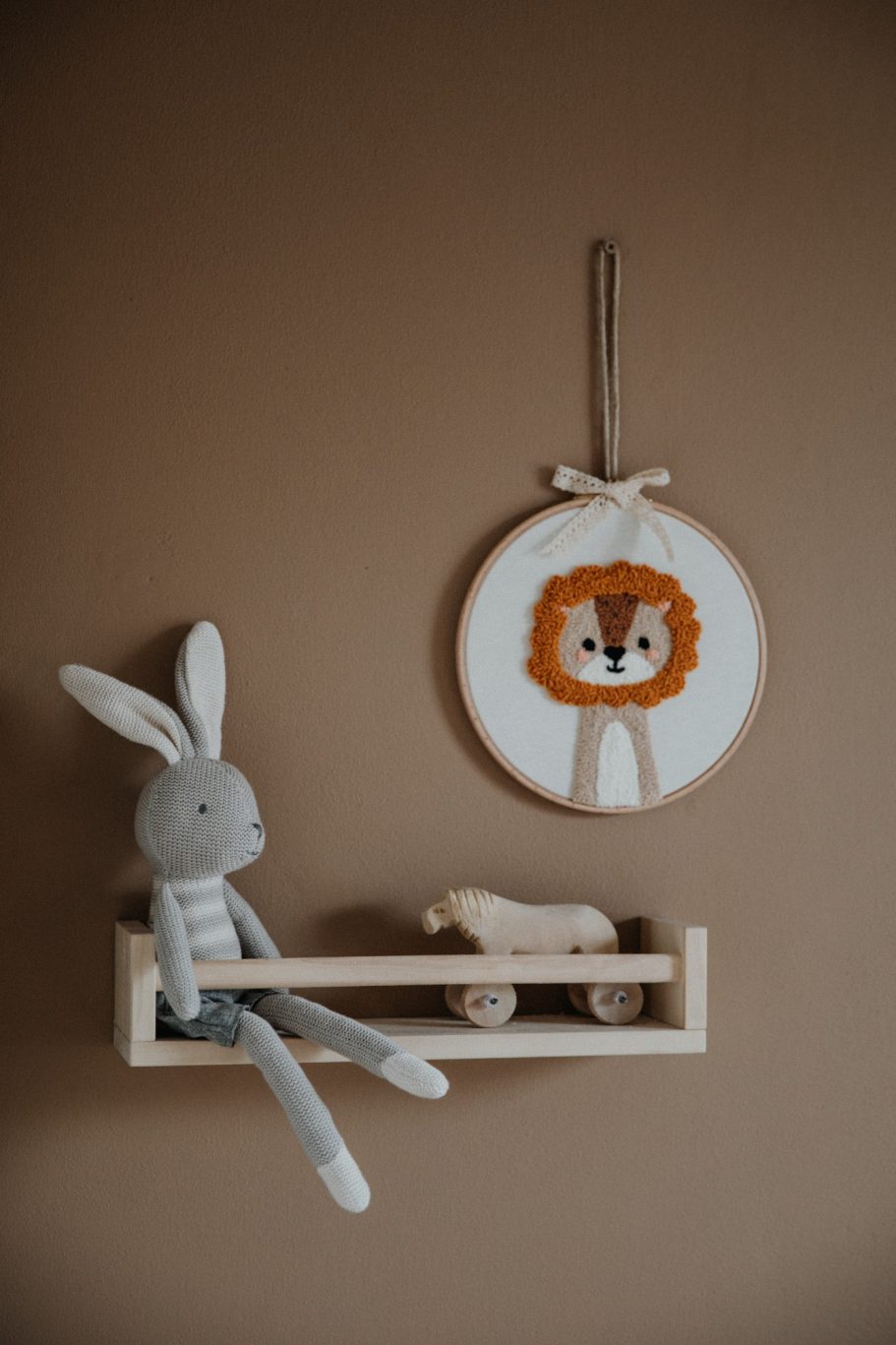 Grijze konijnenkruik met een leeuwenkop op een muurplank tegen een bruine achtergrond.