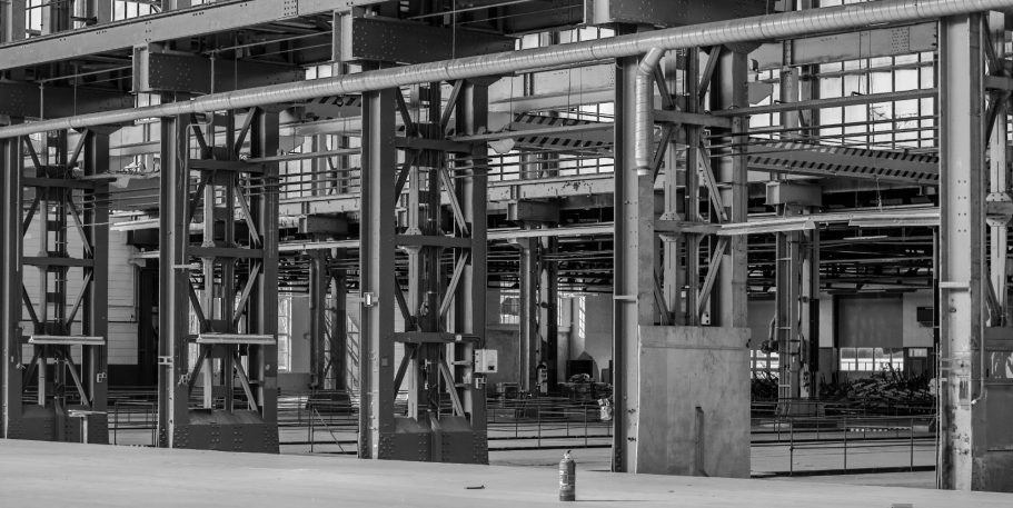 Lege industriële ruimte met metalen pilaren en grote ramen, in zwart-wit.
