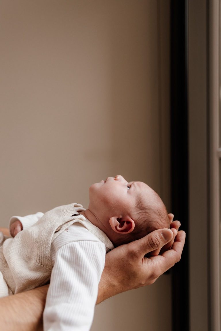 Een hand houdt een baby vast die omhoog kijkt.