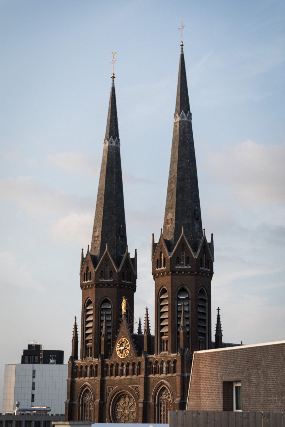 Twee hoge kerktorens met spitse daken en een klok in het midden.