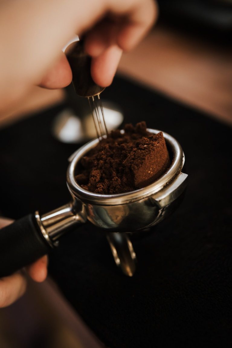 Hand met een tamper die koffie in een portafilter aandrukt.