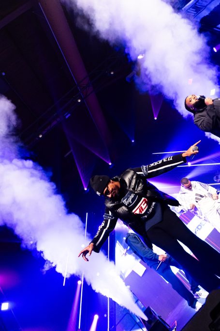 Een artiest performt op een podium met rook en kleurrijke lichten.