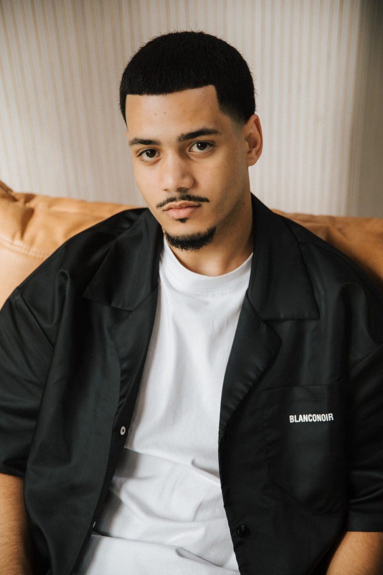 Jongeman met kort haar en een neutrale outfit, zittend op een leren bank.