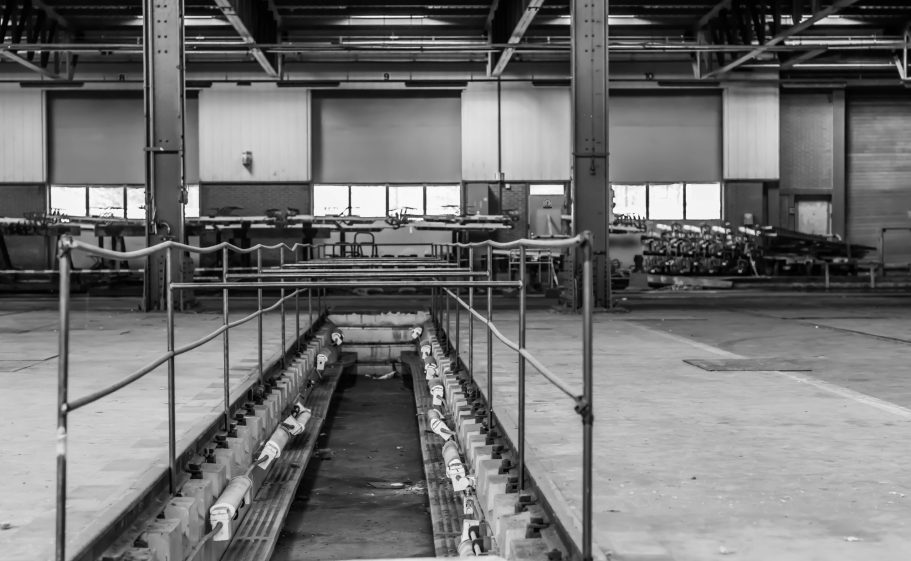 Lege industriële ruimte met lange metalen rail en zichtbare werktafels.