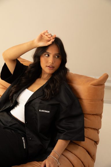 Vrouw met zwart jasje en lange zwarte haren, zittend op een beige bank.