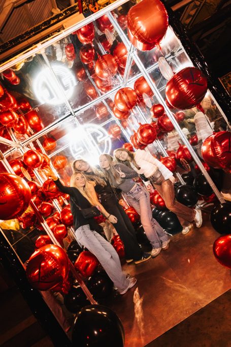 Drie vrouwen poseren tussen rode en zwarte ballonnen. Feestelijke sfeer.