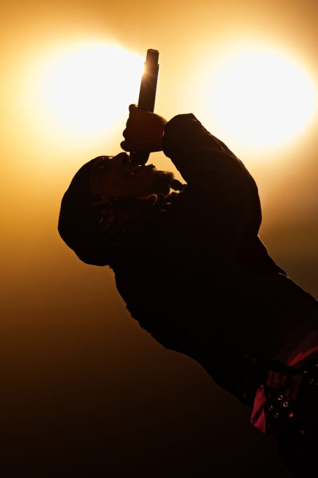 Silhouet van een artiest die met een microfoon zingt tegen een heldere achtergrond.