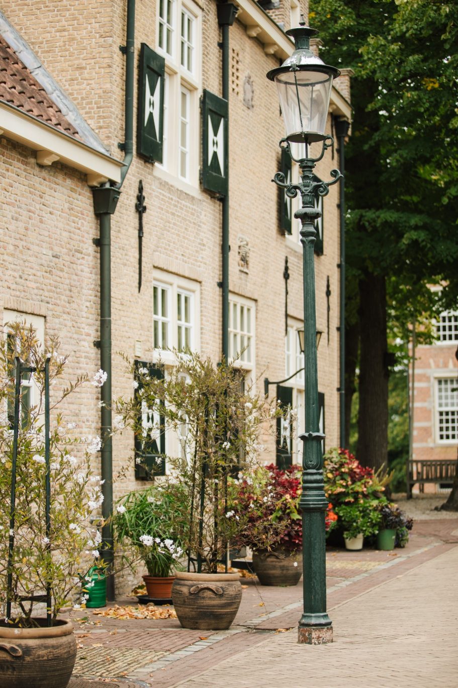 Straat met stenen huizen, bloempotten en een klassieke lantaarnpaal.