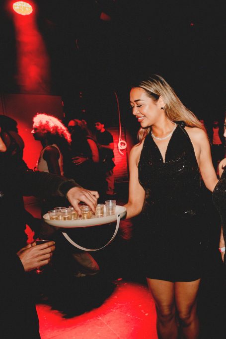 Vrouw in een zwarte jurk serveert drankjes op een feestje met feestverlichting.