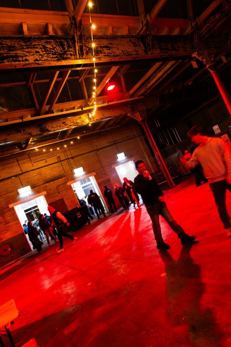 Een grote zaal met rode verlichting, mensen staan bij de open deuren.