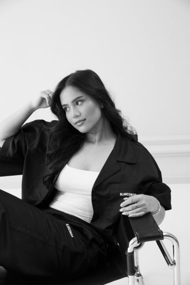 Vrouw met lang zwart haar, zittend, in casual kleding, kijkend en nadenkend.