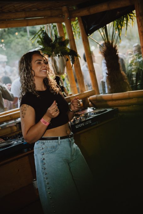DJ H4zel - Geheime Liefde Festival Vrouw met krullend haar in een casual outfit, genietend in een groene omgeving.